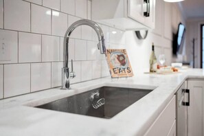 Une cuisine avec un robinet en acier inoxydable, un dosseret de carreaux blancs et un panneau posé sur le comptoir.