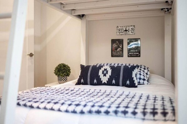 A bed with a patterned bedspread and pillows, a small potted plant, and two framed items on the wall.