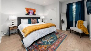 Un dormitorio moderno con una cama grande, una mesita de noche, una silla, un espejo y una alfombra colorida.
