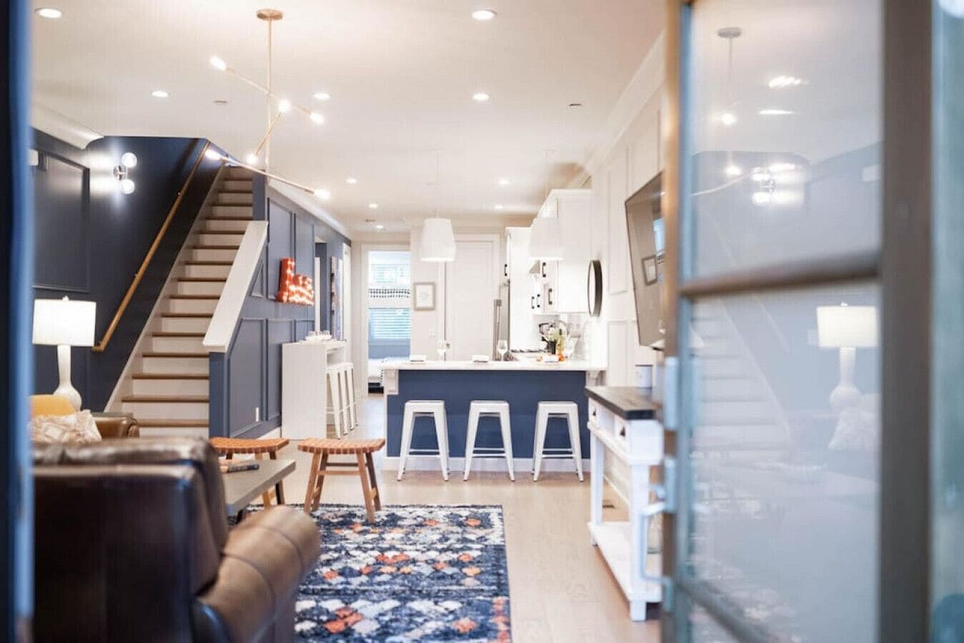 Un intérieur moderne comprenant un escalier, un coin cuisine et un espace salon agrémenté d’un tapis à motifs.
