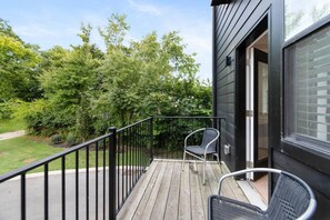 Een houten terras met een metalen hekwerk, een stoel en een gebouw met een donkere gevel.