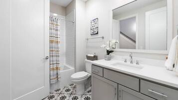 A bathroom with a shower, toilet, vanity, and a large mirror.