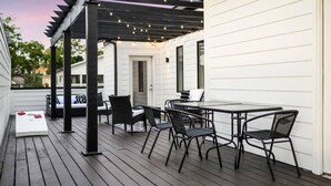 Eine überdachte Terrasse im Freien mit Tisch und Stühlen, Lichterketten und Blick auf ein Haus.