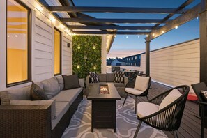 A covered outdoor seating area with a fire feature, wicker furniture, and a wall with hanging lights. - Rooftop & Games Rm in Heart of Downtown - 12 Beds! (Nashville)