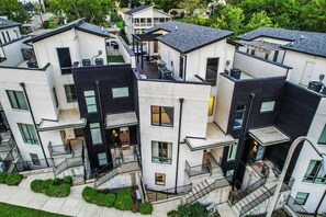 A modern multi-story residential building with a mix of white and dark exterior walls, multiple balconies, and a central courtyard.