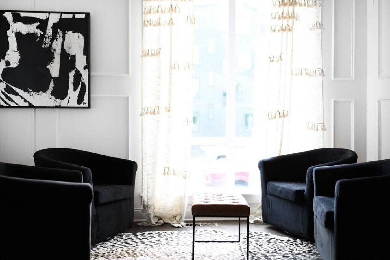 Une pièce décorée d’un tableau abstrait en noir et blanc, de deux fauteuils noirs, d’une petite table et d’un tapis à motifs.