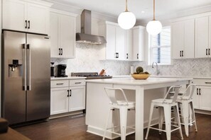 Une cuisine moderne avec des meubles blancs, un réfrigérateur en acier inoxydable, une cuisinière encastrée et des luminaires suspendus.