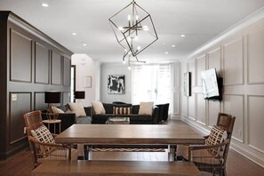 A spacious living room with a large wooden table, two sofas, and a modern chandelier.