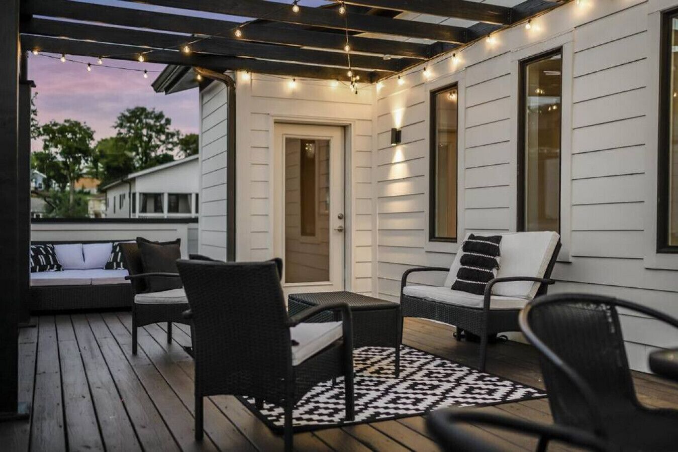A covered outdoor seating area with wicker furniture, a patterned rug, and string lights.