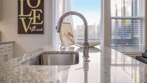 Una cocina moderna con encimera de granito, grifo de acero inoxidable y vistas a la ciudad a través de grandes ventanales.
