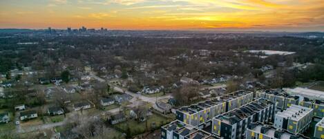 A residential area with modern apartment buildings, a mix of single and multi-story houses, and a distant city skyline during sunset.