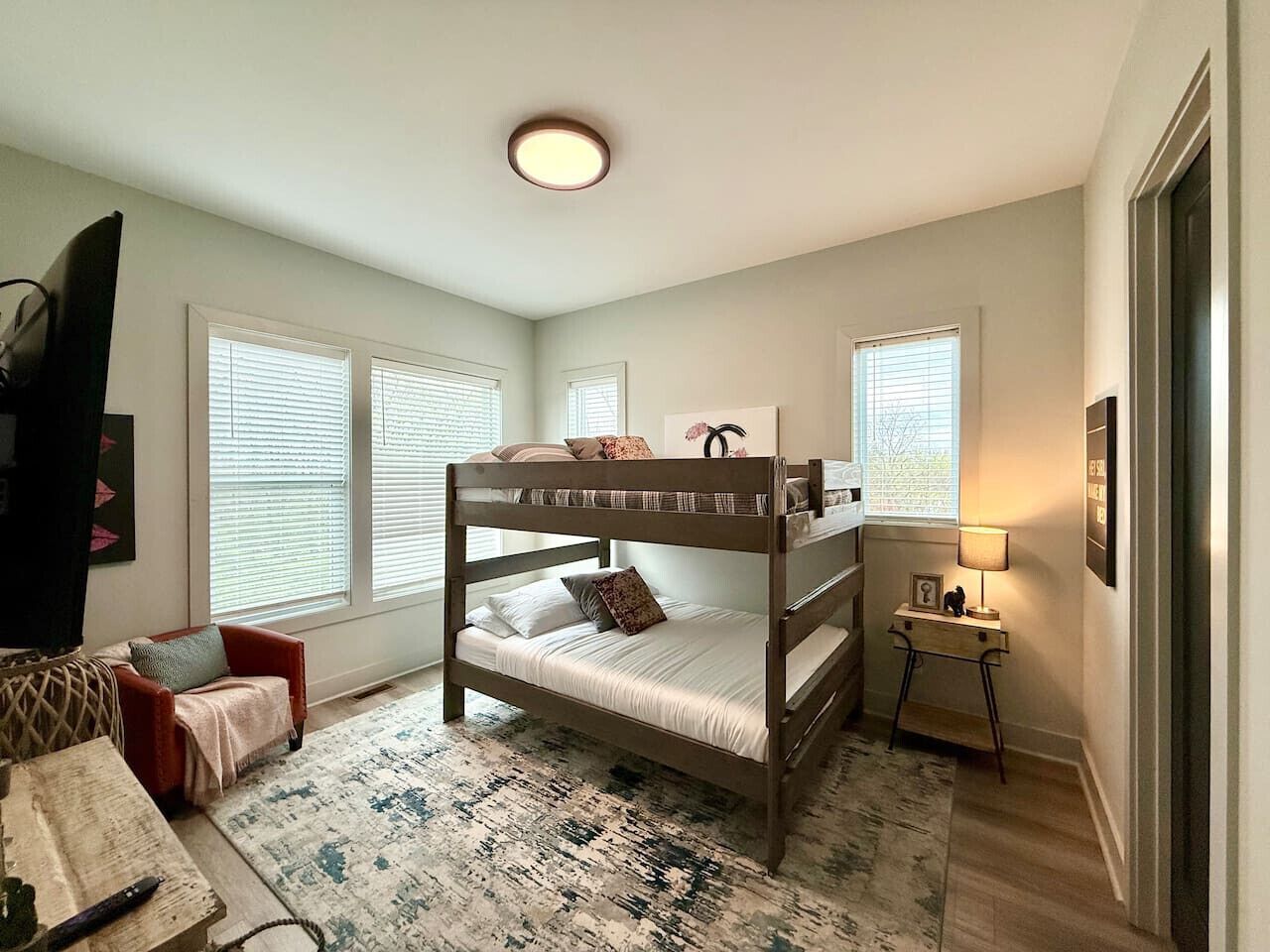 A bunk bed room with a small desk and chair, a rug, and a television.