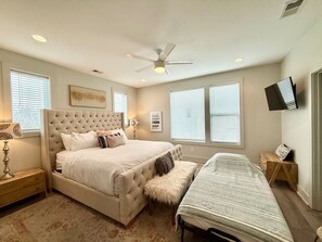 Relax in a spacious bedroom with a large tufted headboard bed, a comfortable bench at the foot, and a flat-screen TV.