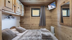 A wooden cabin room with a bed, a window, and a mounted TV. - Modern apartment for 12 with wifi, in the heart of Val Thorens (Val Thorens)