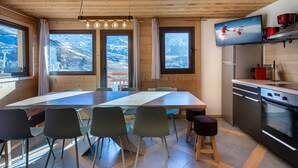 A modern kitchen with wooden cabinetry, a large dining table, and a view of a snowy mountain landscape. - Modern apartment for 12 with wifi, in the heart of Val Thorens (Val Thorens)