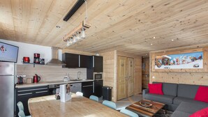 A modern kitchen with wooden cabinets, a dining area with a wooden table and chairs, and a living area with a sofa and red cushions. - Modern apartment for 12 with wifi, in the heart of Val Thorens (Val Thorens)