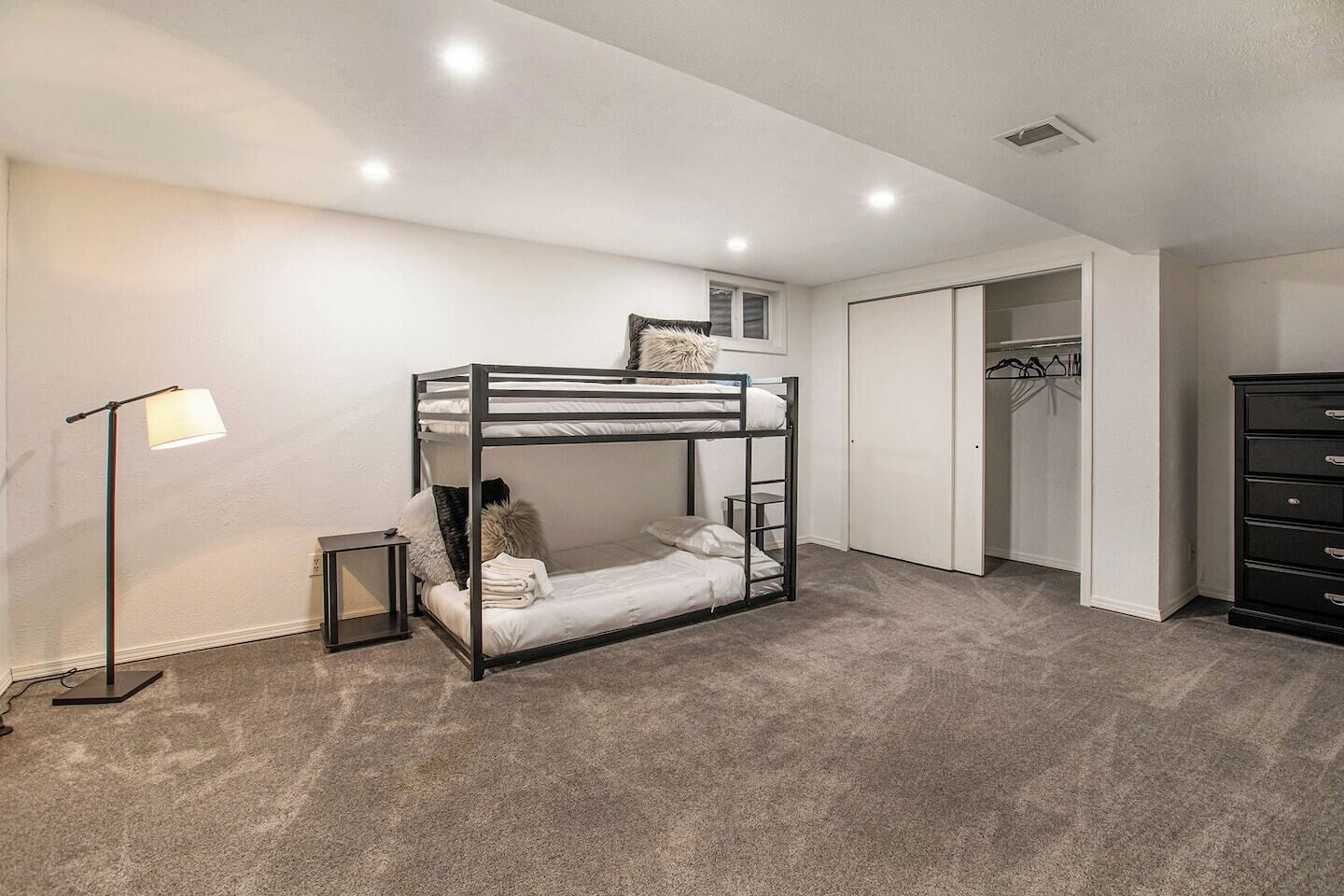 A bunk bed room with a wardrobe, a dresser, and a lamp.