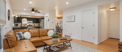 A modern living room with a leather sectional sofa, a coffee table, and a dining area in the background.