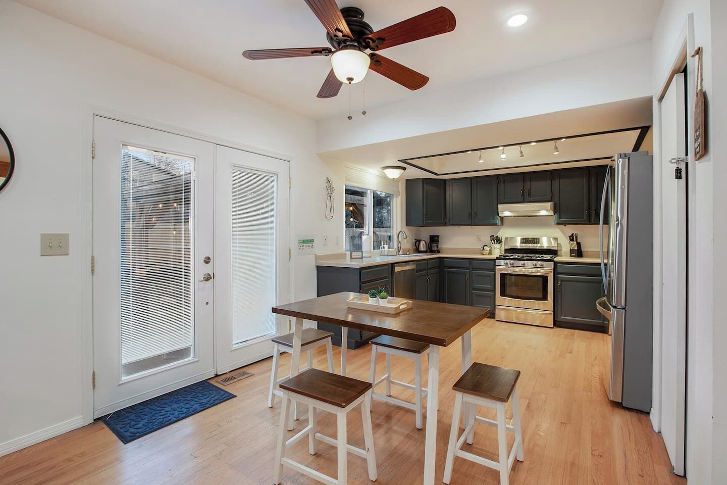 A modern kitchen with a central island, dark cabinets, stainless steel appliances, and a ceiling fan.