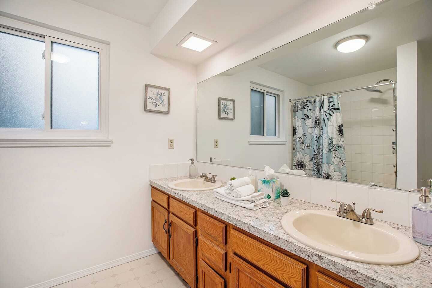 A bathroom with two sinks, wooden cabinets, a large mirror, and a shower curtain with a floral pattern.