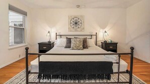 A bedroom with a four-poster bed, two bedside tables, a ceiling fan, a window, and a wall-mounted artwork.