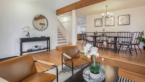 A spacious living area with a dining table, chairs, a sofa, and a staircase leading to another level.