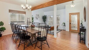 A spacious dining area with a wooden table and chairs, a chandelier, and a view of the city through large windows.