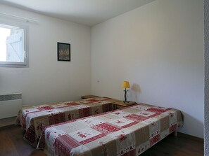 Una habitació amb dos llits individuals, una taula petita, una làmpada, una finestra i un quadre a la paret.