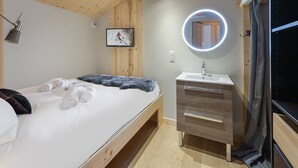 Makuuhuoneessa on sänky, yöpöytälamppu, televisio, peili ja puinen lipasto.