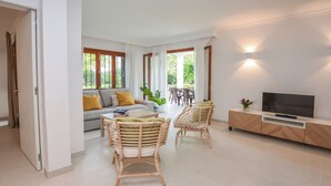 En moderne stue med en sofa, to fletstole, et spisebord og et fjernsyn på et træskab.