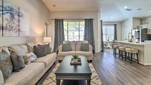 A living room with a sofa, coffee table, and a view of the kitchen. - 5 Mi to Disney World: Retreat w/ Pool & Lanai! (Kissimmee)