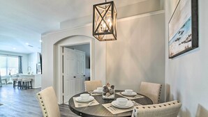 A dining area with a round table set for six, surrounded by upholstered chairs. A decorative centerpiece is on the table, and a wall-mounted light fixture hangs above. - 5 Mi to Disney World: Retreat w/ Pool & Lanai! (Kissimmee)