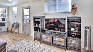 Een woonkamer met een grote flatscreen-tv, een donker houten tv-meubel met glazen deuren, een geweven bankje en een radiator.