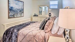Een slaapkamer met een bed, nachtkastje, lamp, kapstok en een schilderij aan de muur.