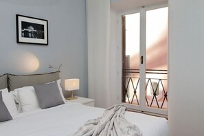 Ein Hotelzimmer mit einem Bett, einem Nachttisch mit Lampe, einem gerahmten Bild an der Wand und einem Balkon mit Geländer.