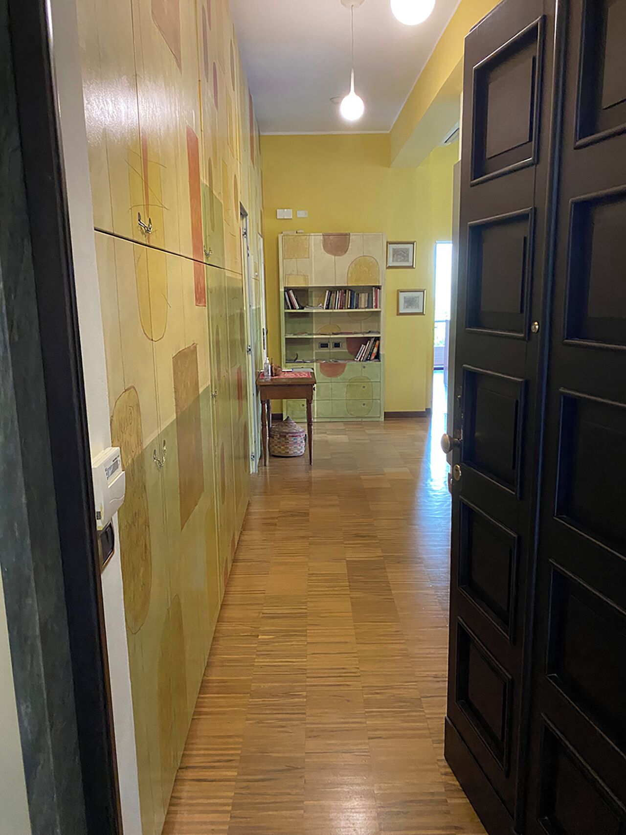 A hallway with wooden flooring, a bookshelf, and a door.