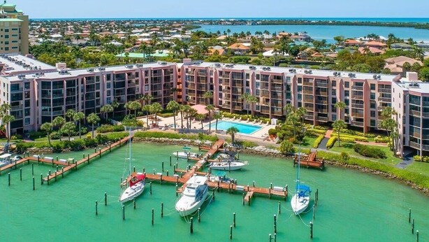 Un port de plaisance avec des bateaux amarrés, une piscine et un hôtel à plusieurs étages doté de balcons.