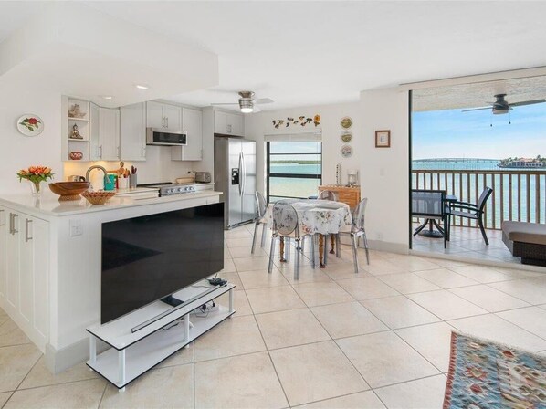 A modern kitchen with a TV, dining area with chairs, and a balcony with a view of the sea. - Waterfront 1BR condo in Marco Island with pool, Wi-Fi, and marina access. (Marco Island)