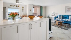 Une cuisine moderne avec des meubles blancs, un grand îlot central et une vue sur la mer par la fenêtre.