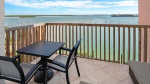 Un balcon avec une table et des chaises, donnant sur une étendue d’eau dont on aperçoit la côte au loin.