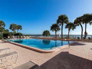 A swimming pool with lounge chairs and palm trees, surrounded by a brick patio.