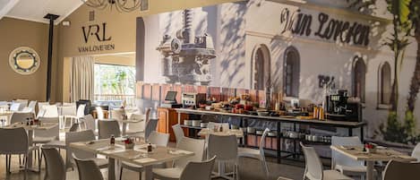 Un restaurante con varias mesas y sillas, una zona de bar con distintos productos alimenticios y una máquina de café, además de un mural en la pared.