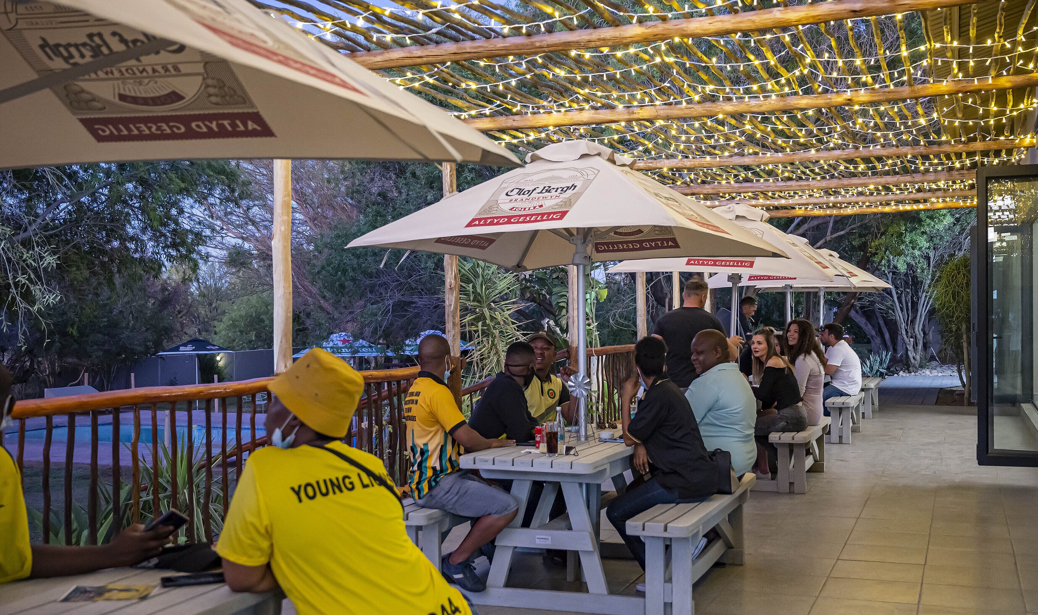 A covered outdoor seating area with tables and umbrellas, surrounded by greenery.