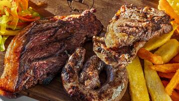 A wooden cutting board with grilled steak, sausage, and French fries.