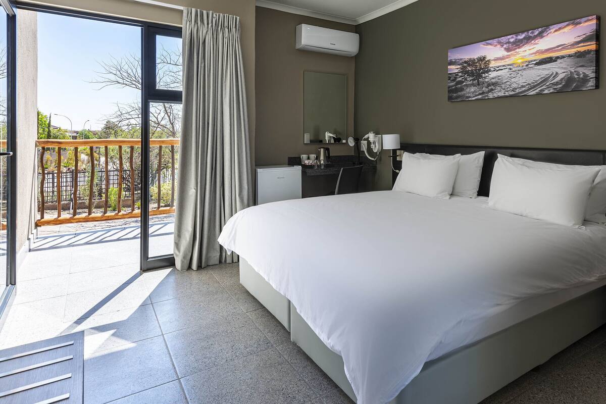 A hotel room with a large bed, a bathroom with a mirror, and a balcony with a view of the outdoors.