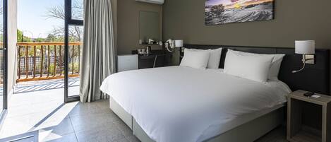 A hotel room with a large bed, a bathroom with a mirror, and a balcony with a view of the outdoors.