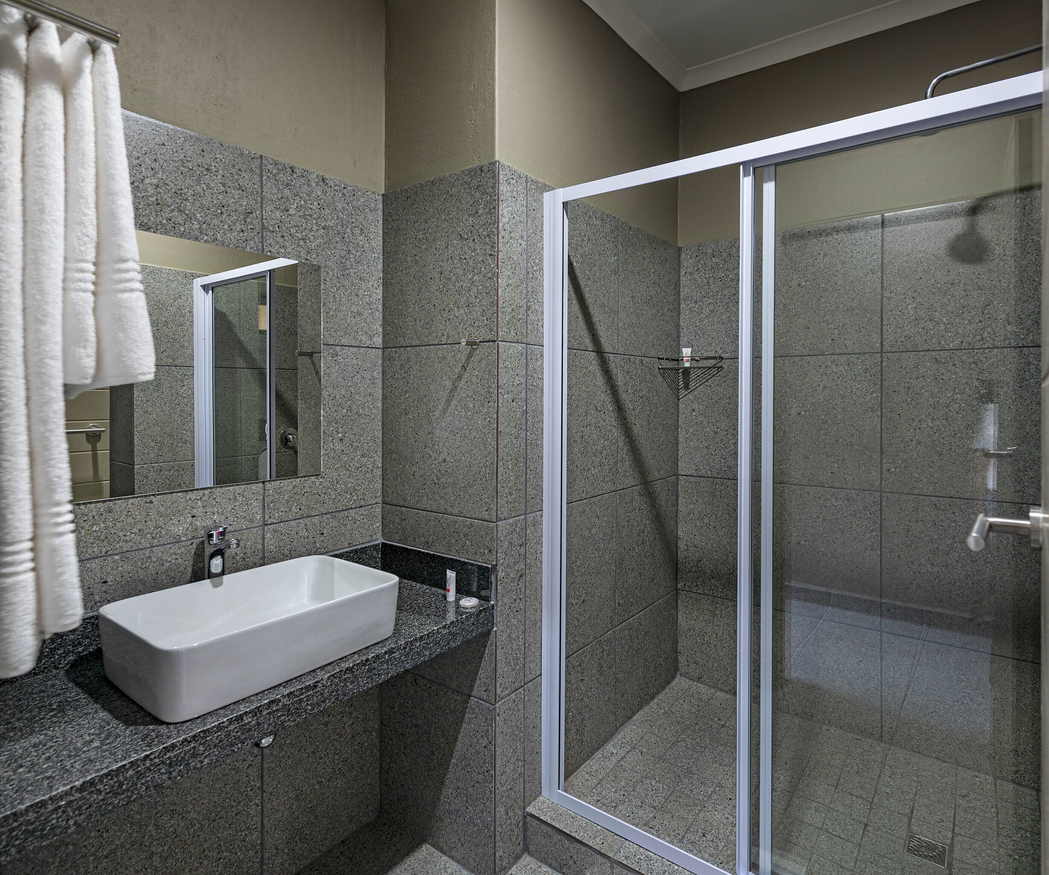A modern bathroom with a white sink, granite countertop, and a glass shower enclosure.
