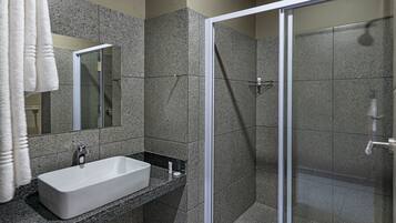 Une salle de bain moderne avec un lavabo blanc, un comptoir en granit et une cabine de douche en verre.