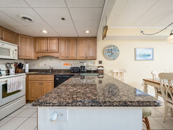 A kitchen with granite countertops, wooden cabinets, a microwave, and a coffee maker.