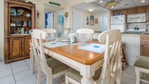 A dining area with a wooden table and four chairs, a wooden cabinet with various items, and a kitchen area with a microwave and refrigerator.